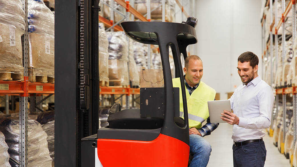 仓库中男子看着平板电脑交谈，其中一人坐在叉车上